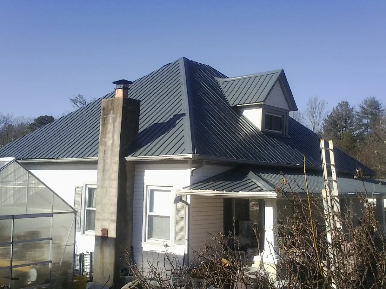 Dark blue standing seam metal roof on a white farmhouse with dormer — Slate & Tile Roof Repair by Roofing Brothers in Beloit