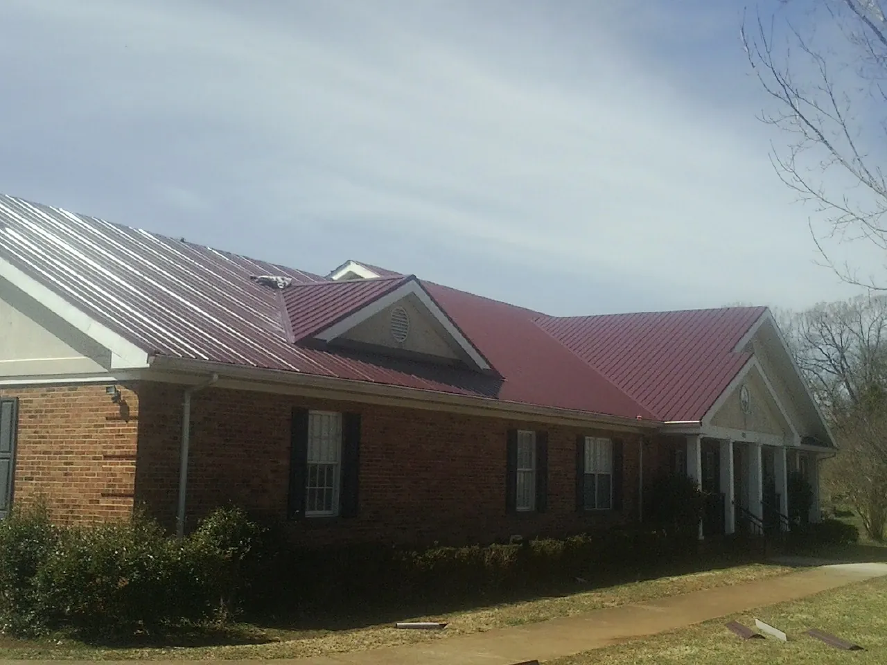Red metal roof with gabled entries on a long brick building, from a Hail Damage Roof Repair job in Beloit