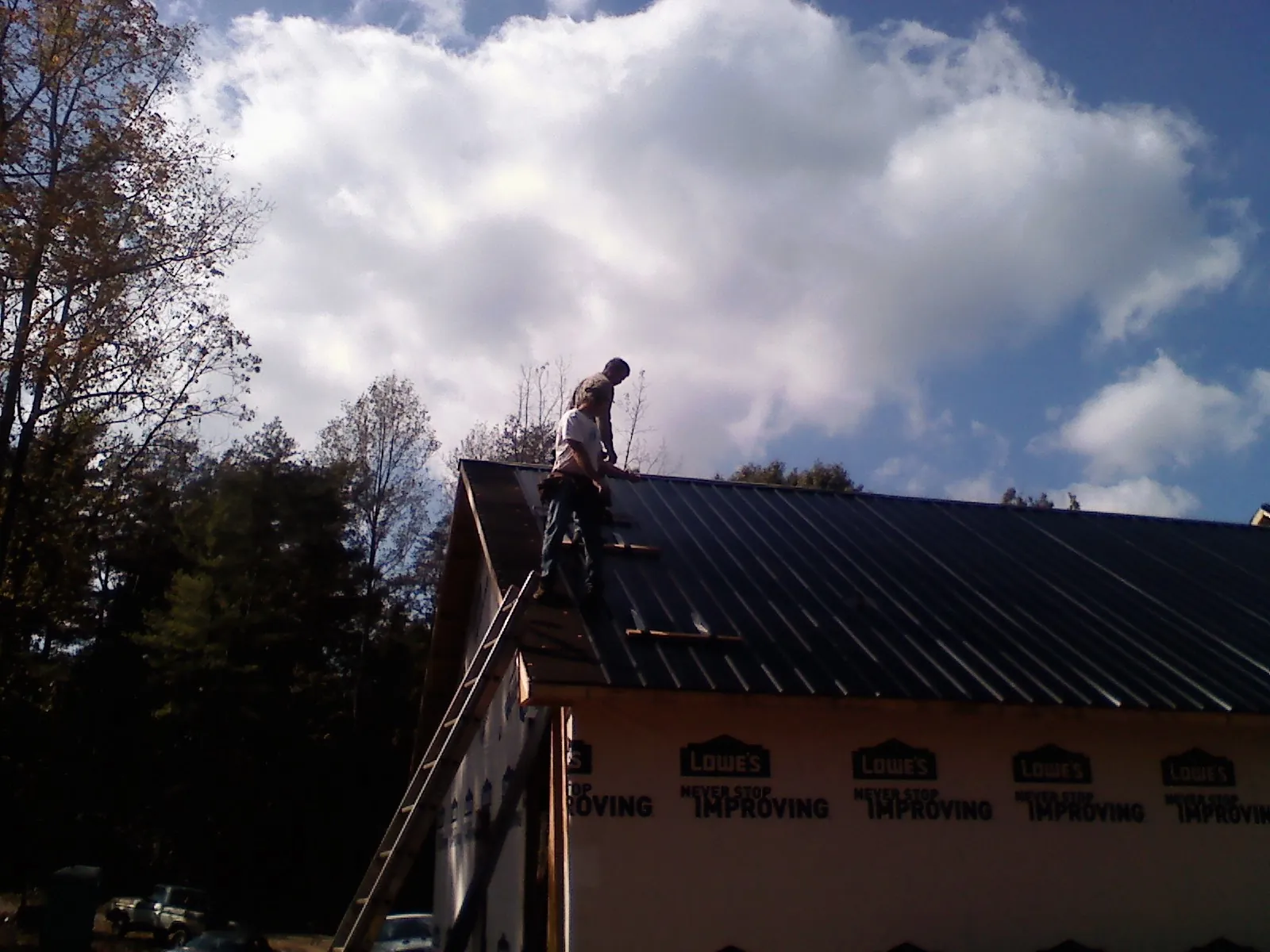 Roofer fastening dark metal panels high against a cloudy sky, from a Roof Inspection job in Beloit